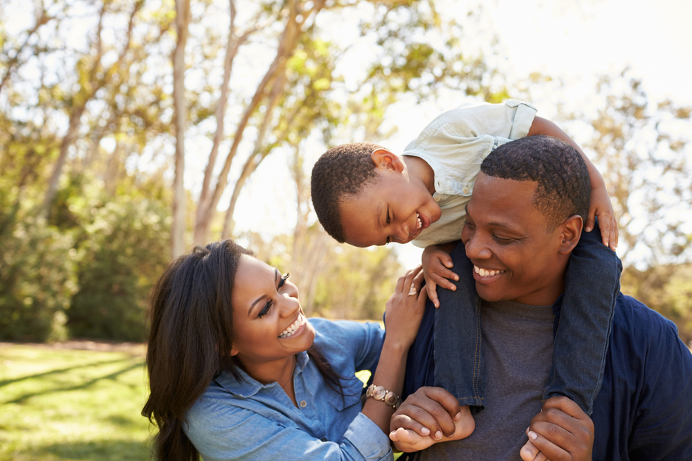 Parents,Carrying,Son,On,Shoulders,As,They,Walk,In,Park